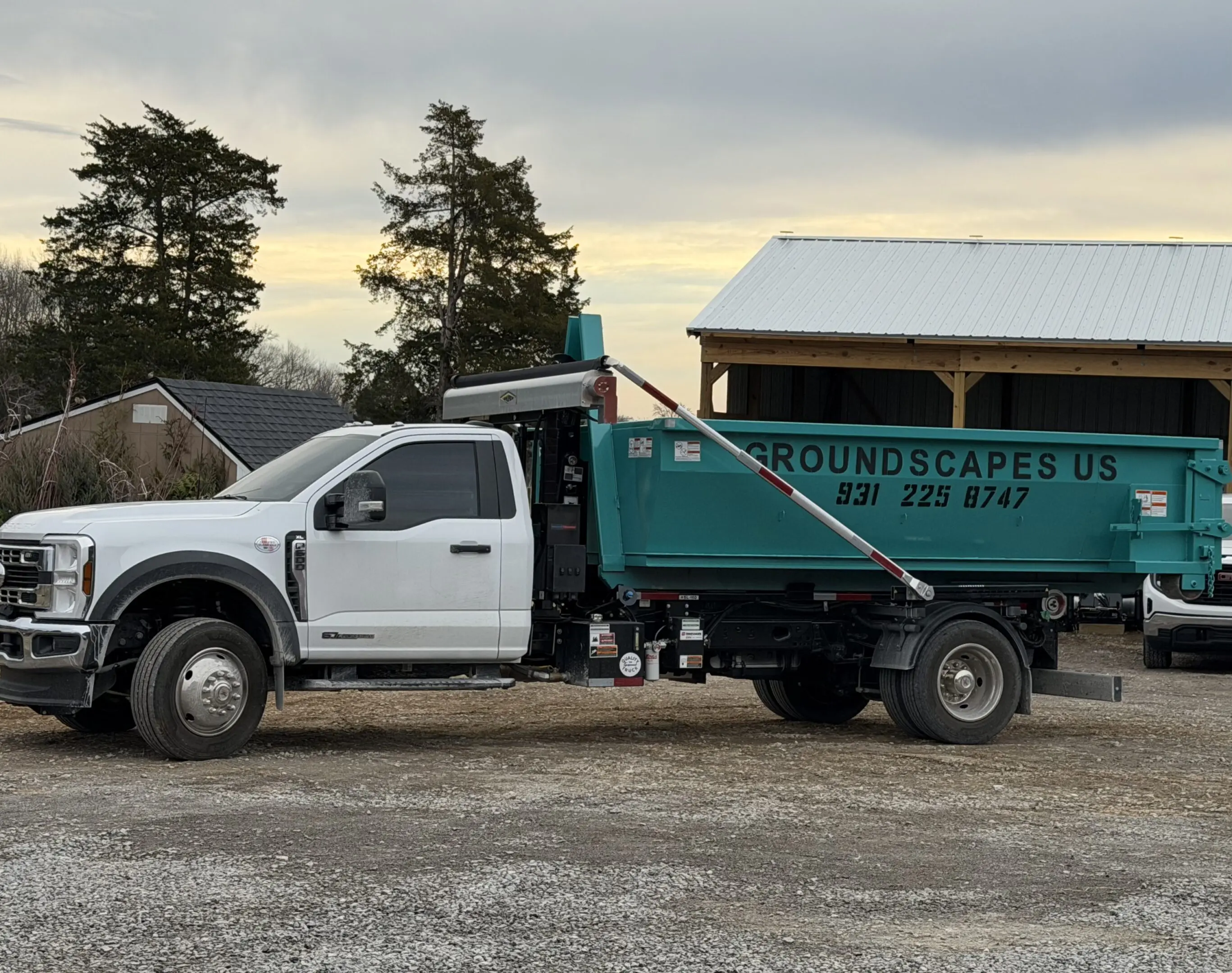 A white and green landscaping truck parked on a gravel driveway at sunset.