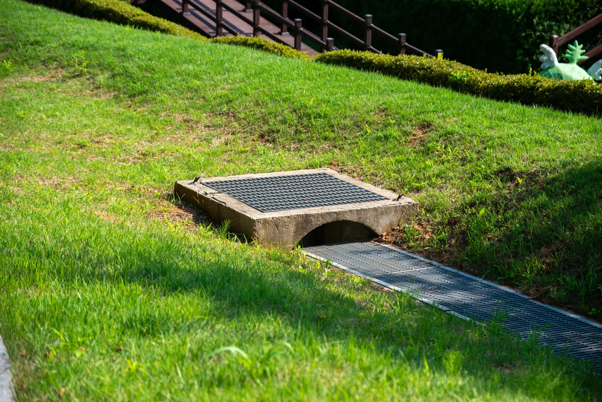 A stone drainage outlet on a grassy hill with a wooden fence in the background.