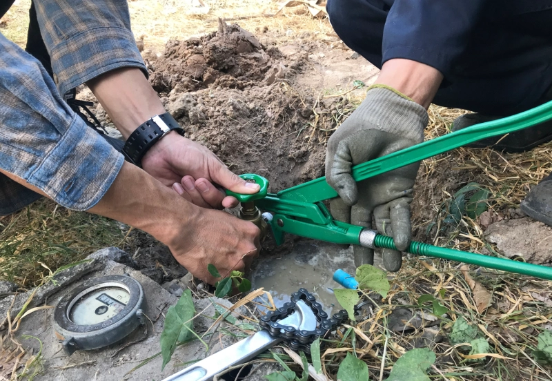 Two people using green bolt cutters to cut a cable outdoors.