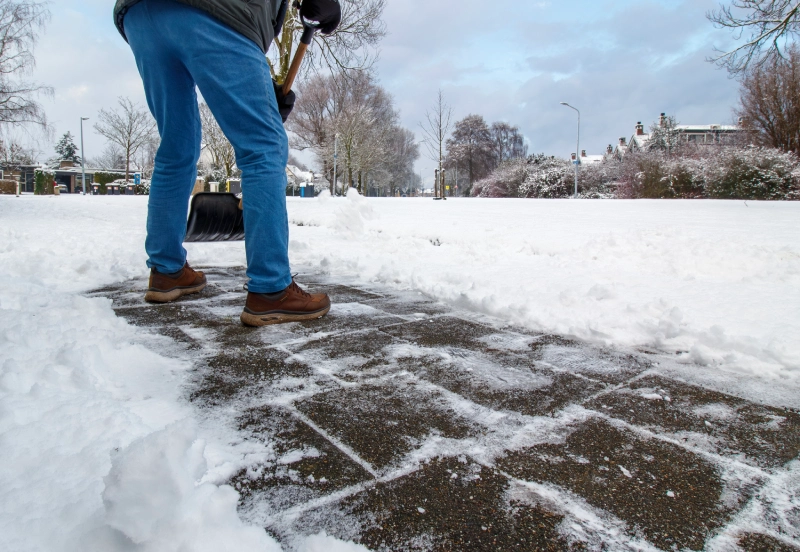 Person standing on a snowy sidewalk with snow-covered surroundings.