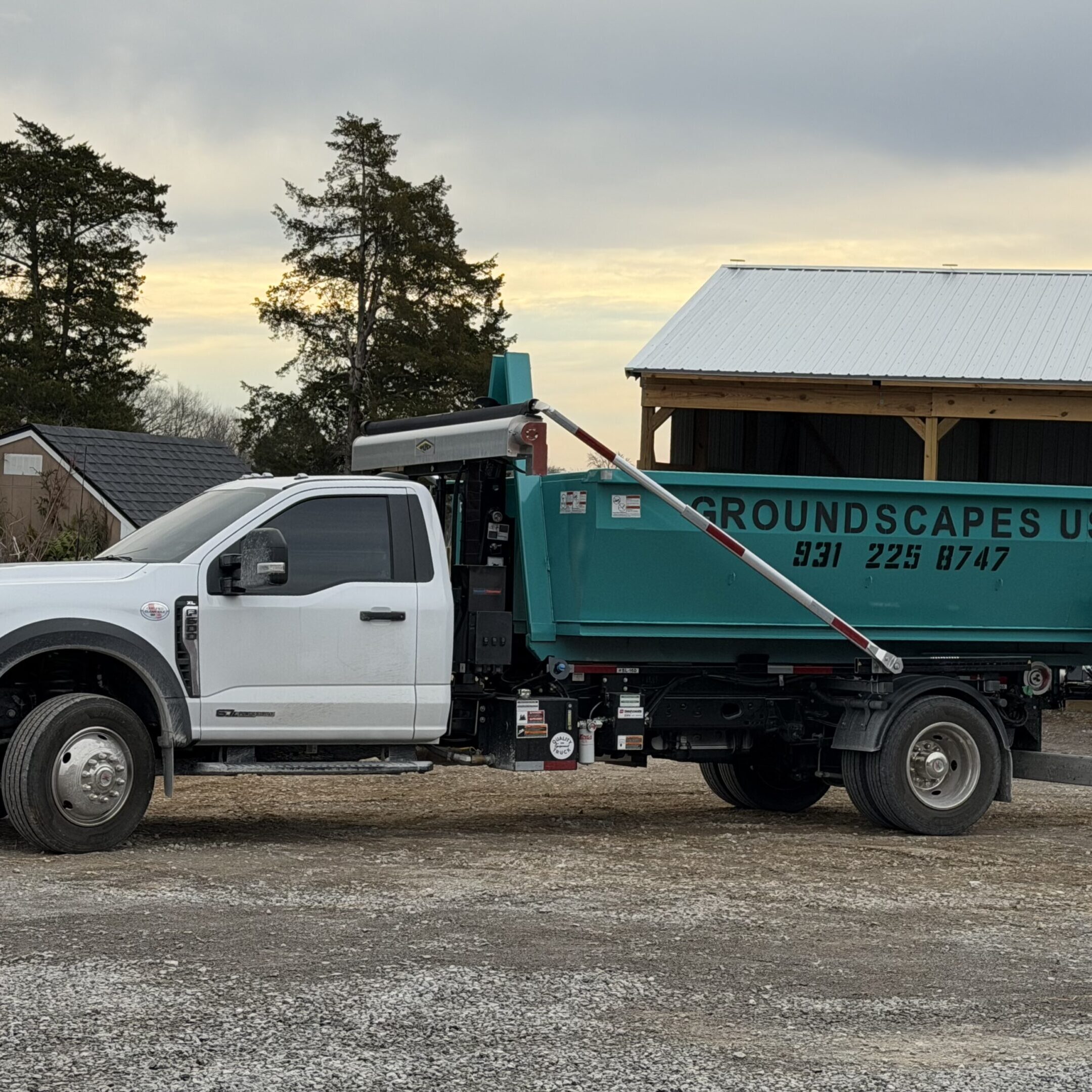 A white and green landscaping truck parked on a gravel driveway at sunset.