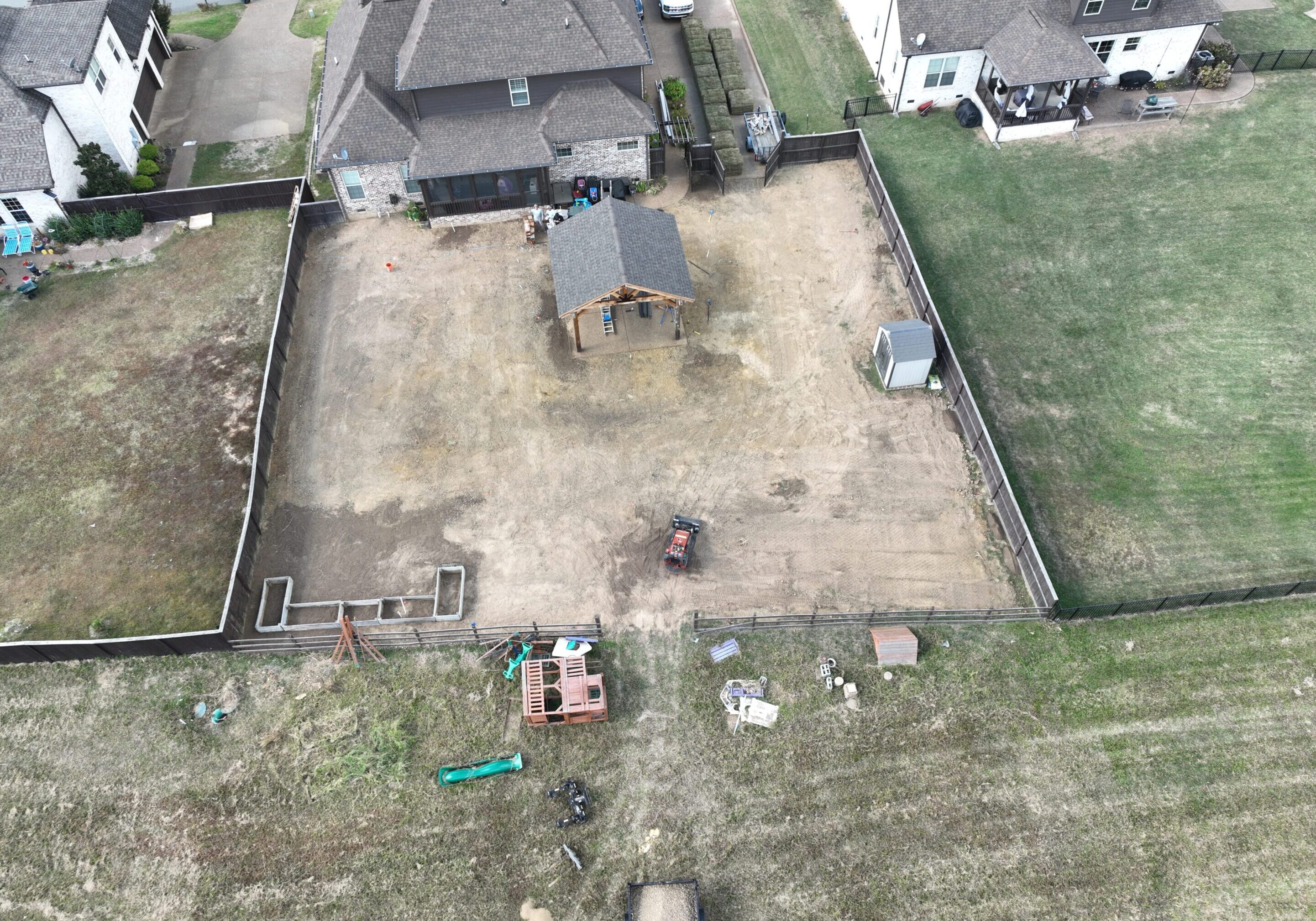 A backyard with bare soil and scattered equipment surrounded by fences.